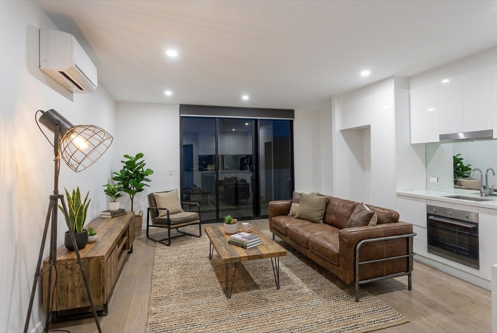 The same room virtually staged by ProMyPhoto — leather sofa, timber coffee table, rug, lamp and plants added
