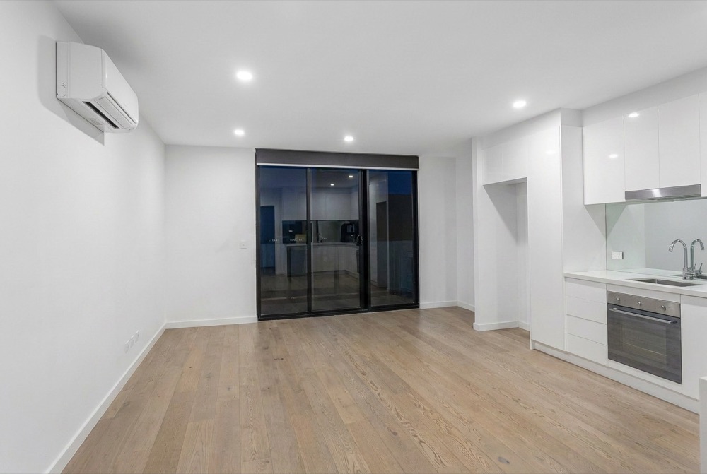 An empty open-plan living and kitchen area with bare floors and walls
